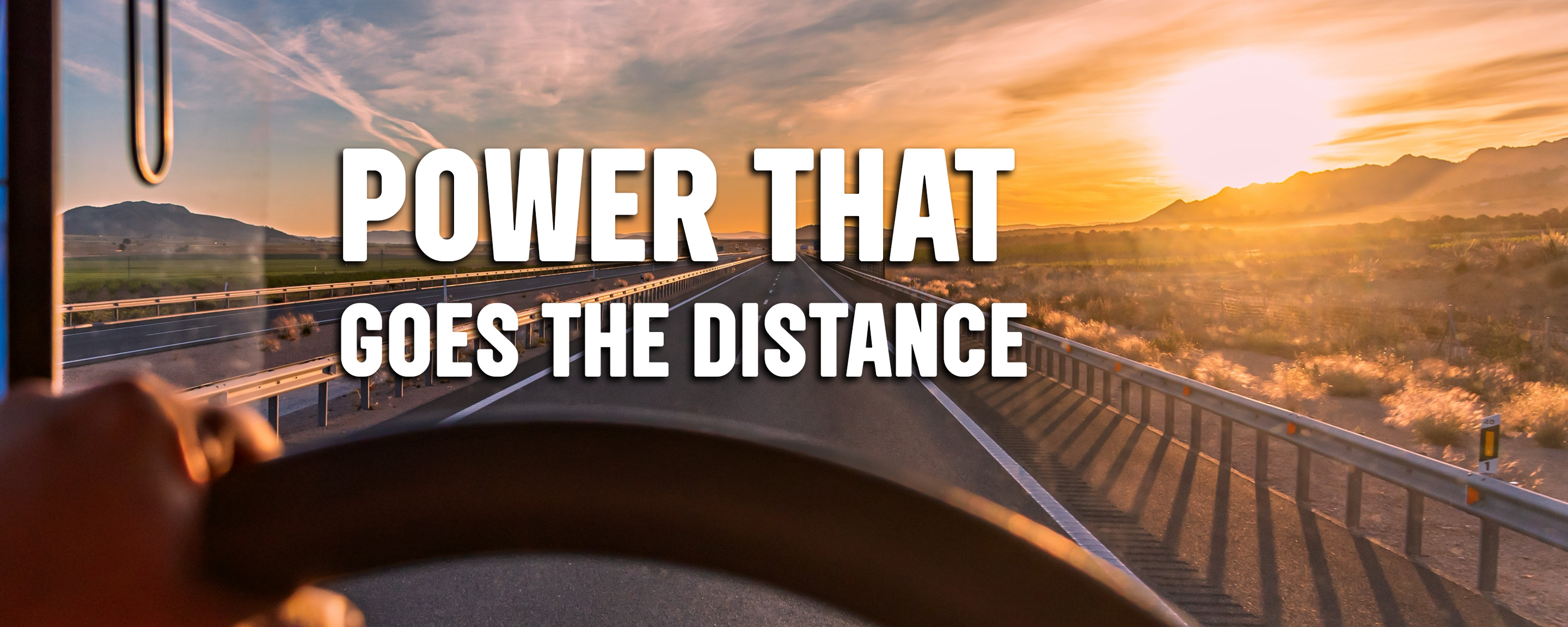 driver's hands on steering wheel with "Power That Goes The Distance" in windshield