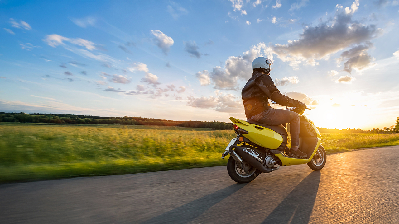 person riding scooter on the road in front of a sunset