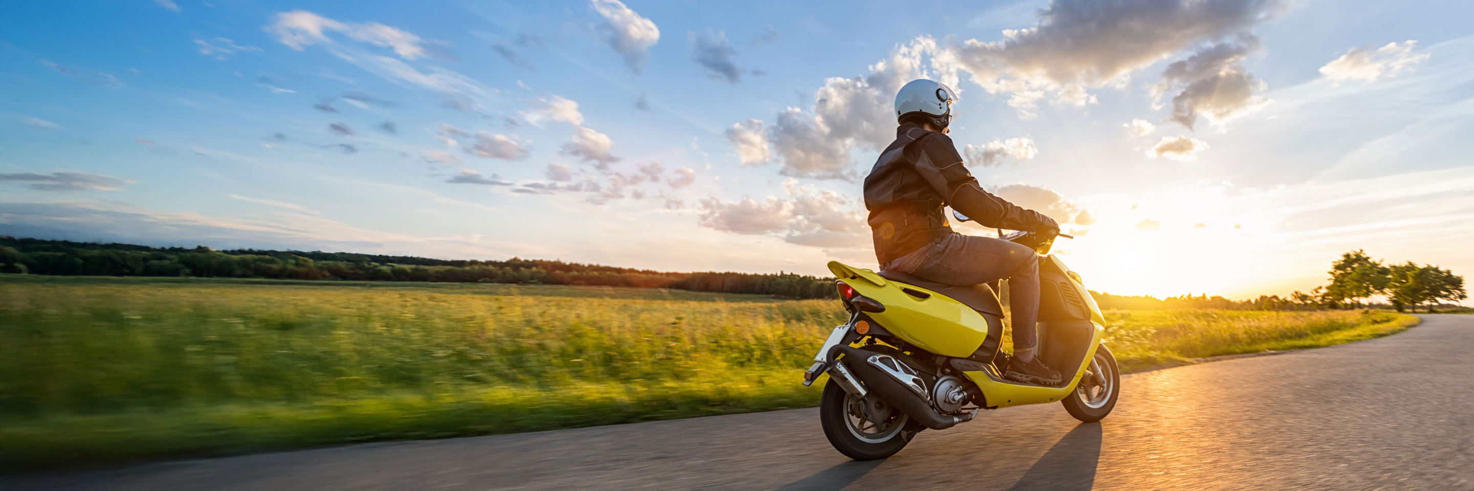 person riding scooter on the road in front of a sunset