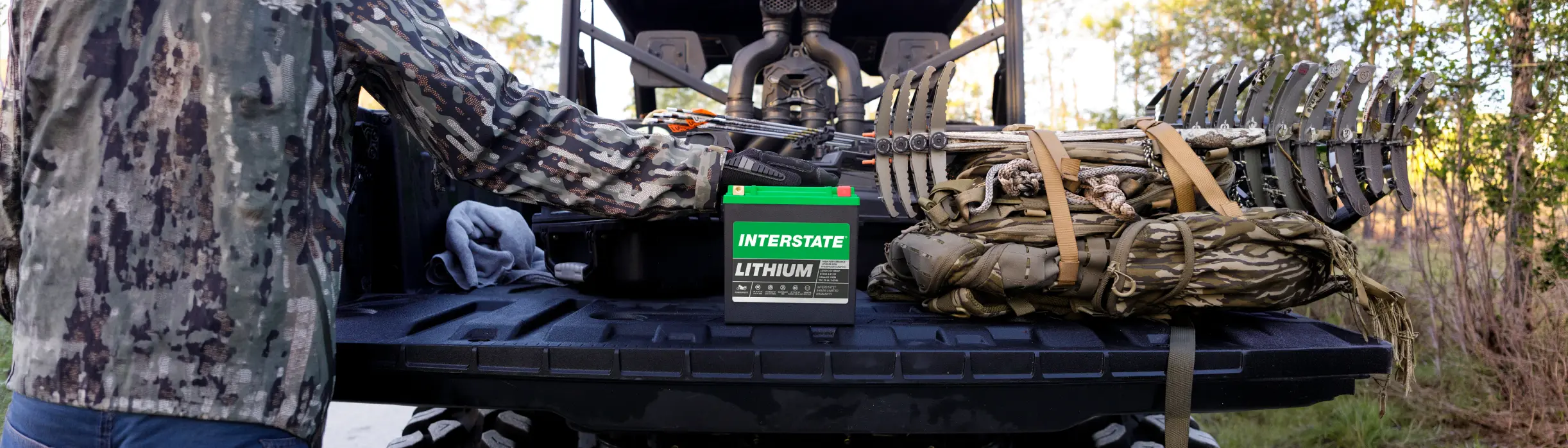 A person driving a motorcycle down a road with an Interstate lithium battery in bottom right corner