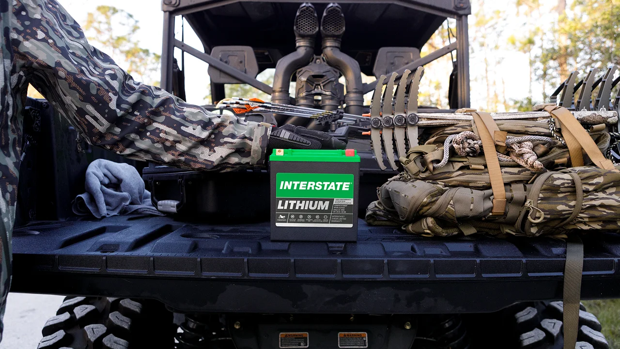 A person driving a motorcycle down a road with an Interstate lithium battery in bottom right corner
