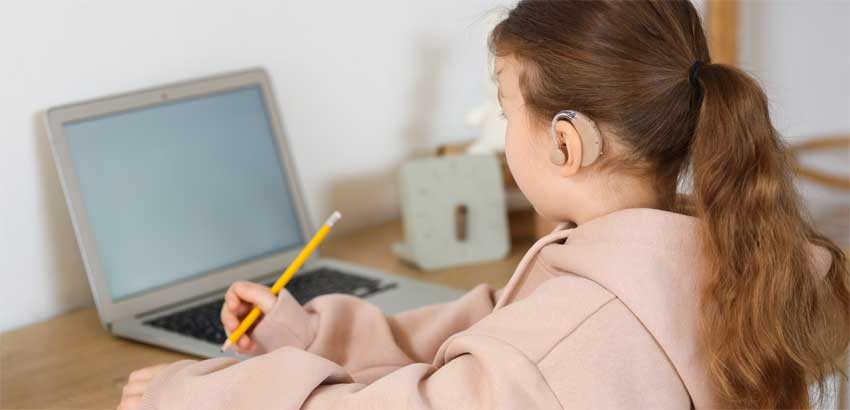 young girl doing homework with a hearing aid