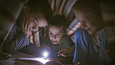 Children Reading a Book with a Flashlight Under a Blanket Fort