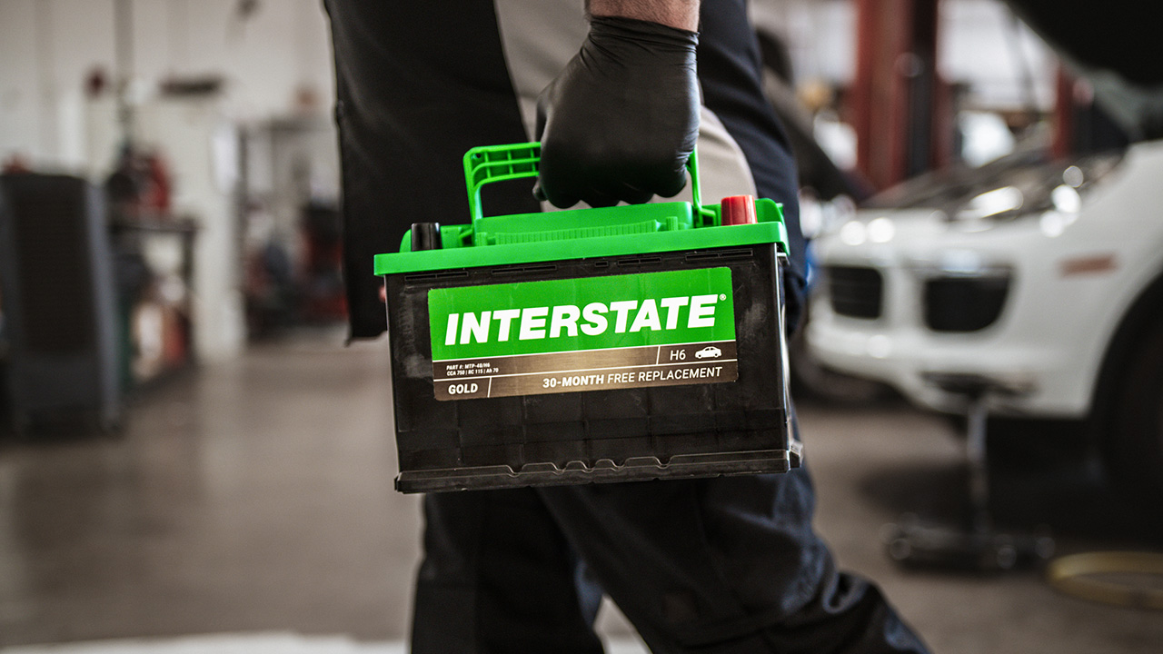 mechanic holding Interstate battery in a car shop